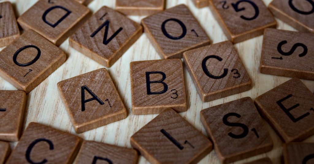 Scattered wooden Scrabble tiles showcasing letters and typography on light wooden surface.